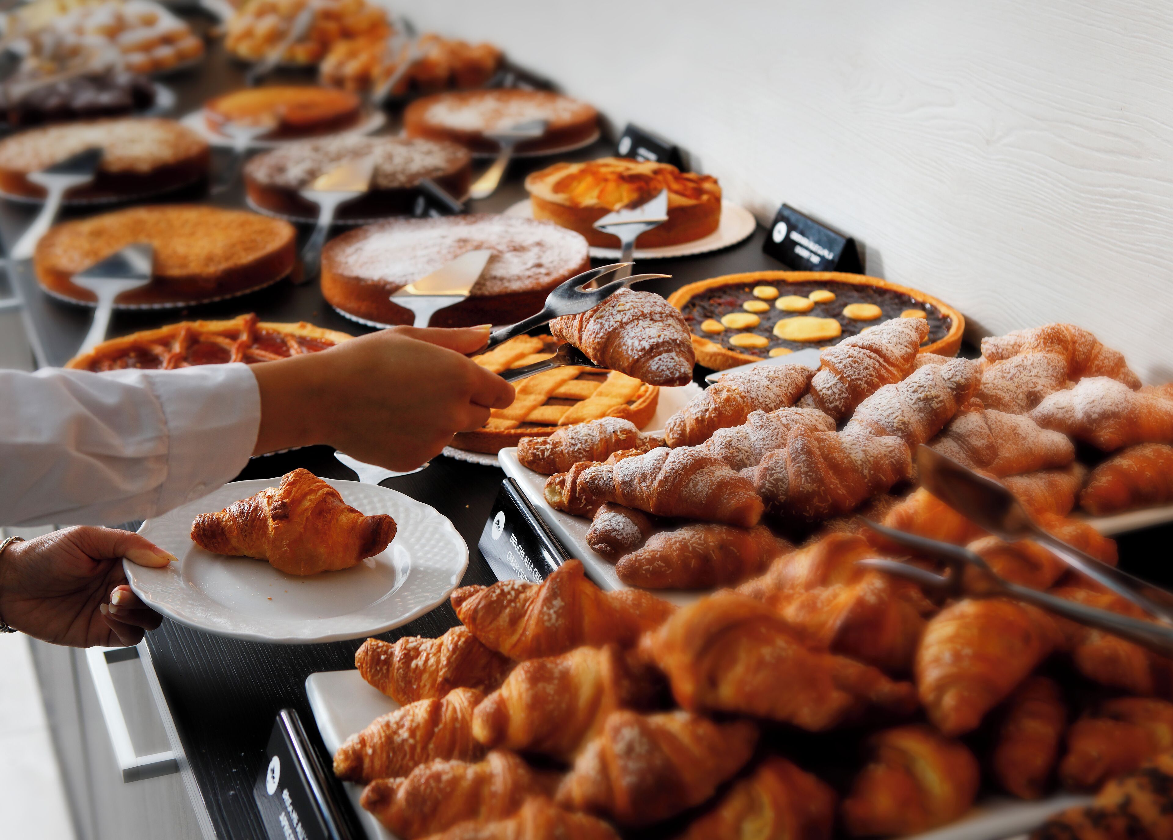 Een buffet met diverse gebakjes en desserts, waaronder croissants en taart.