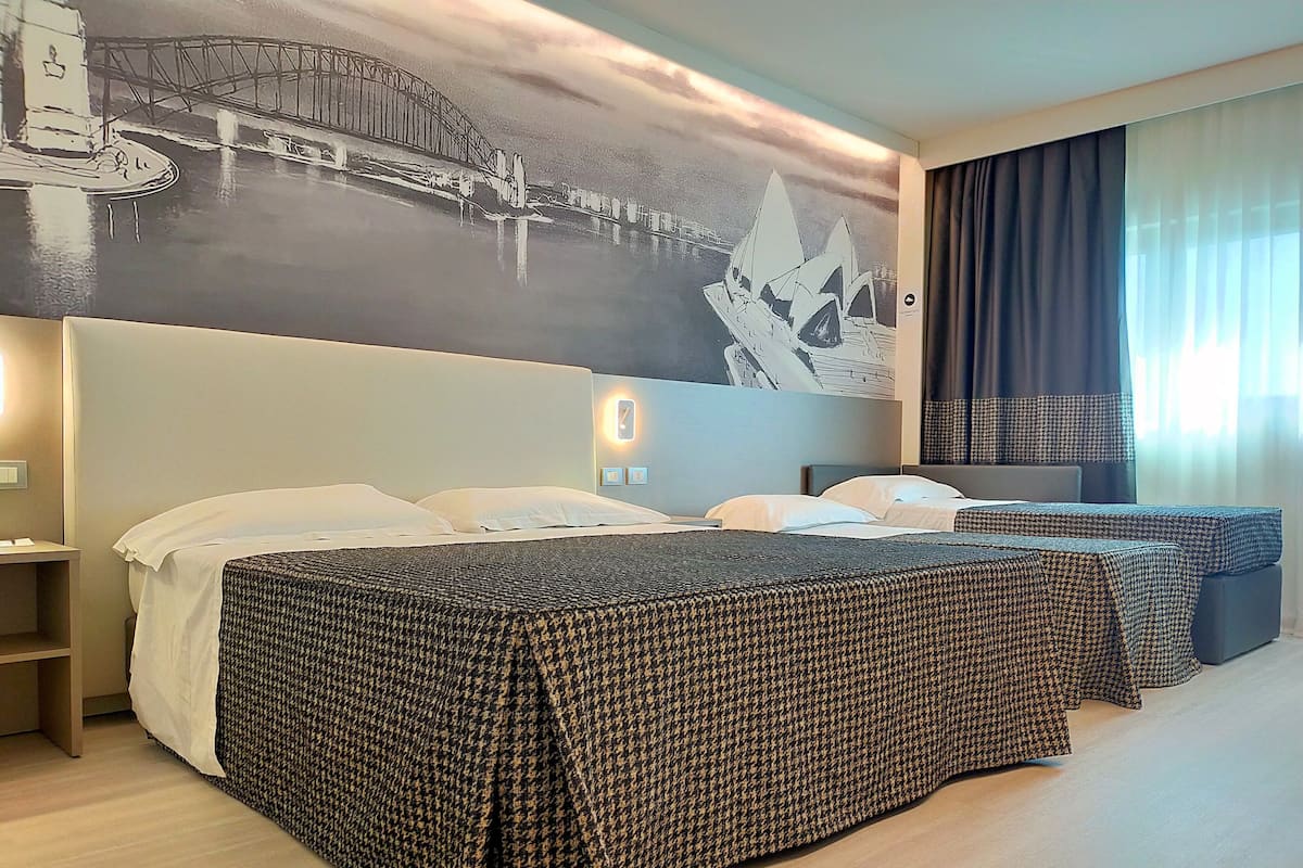 Une chambre d’hôtel avec un grand lit, un lit plus petit, un canapé, une fresque murale et une fenêtre avec des rideaux.