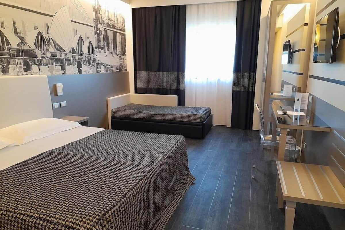 Une chambre d’hôtel avec deux lits, un bureau, une chaise, une télévision et une grande fenêtre avec des rideaux.