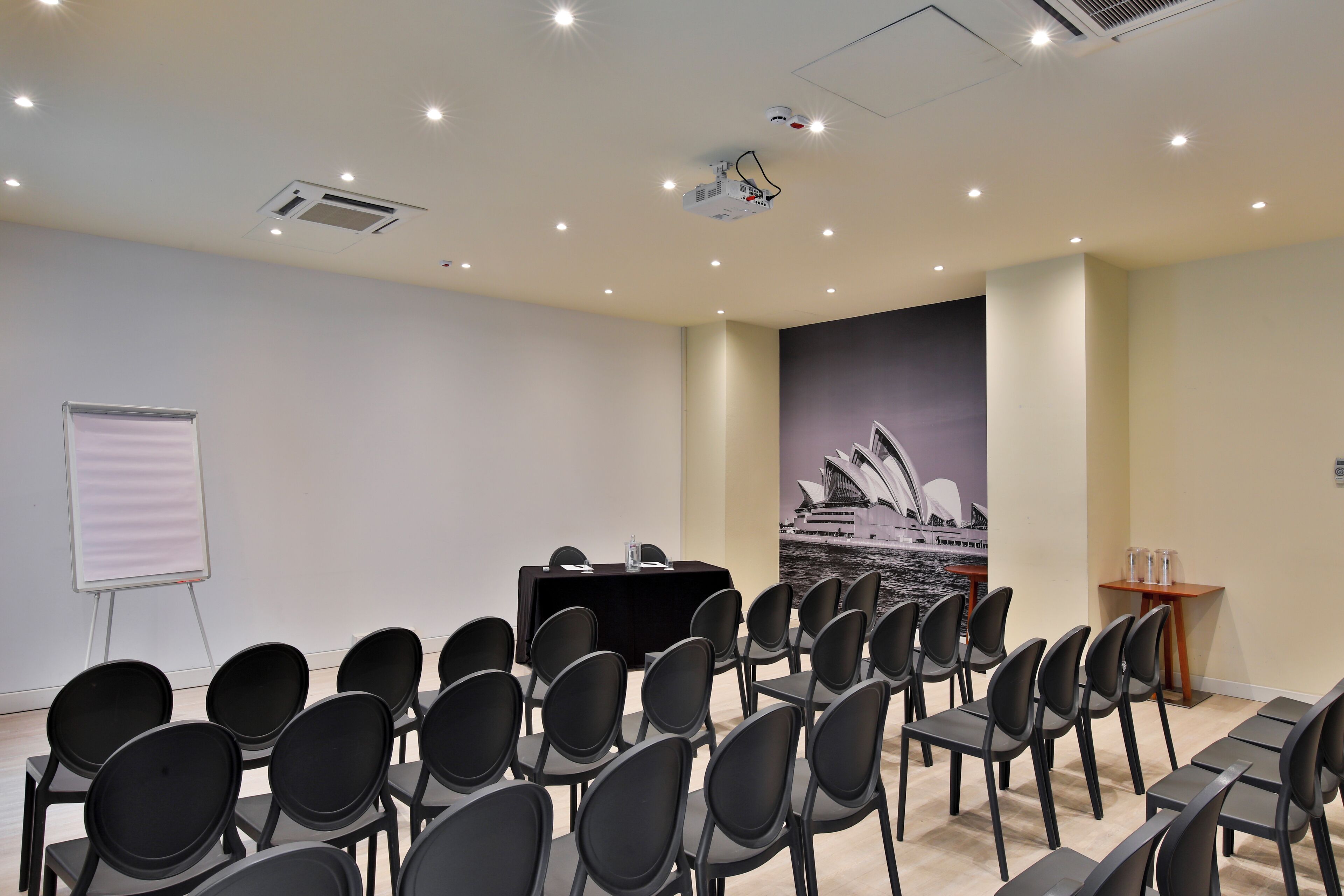 Una sala conferenze con file di sedie, un proiettore, una lavagna e un murale con la Sydney Opera House.