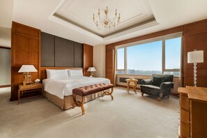 A spacious hotel bedroom with a large bed, a bench, a chair, and a view of the city. - Shangri-La Huhhot (Hohhot)