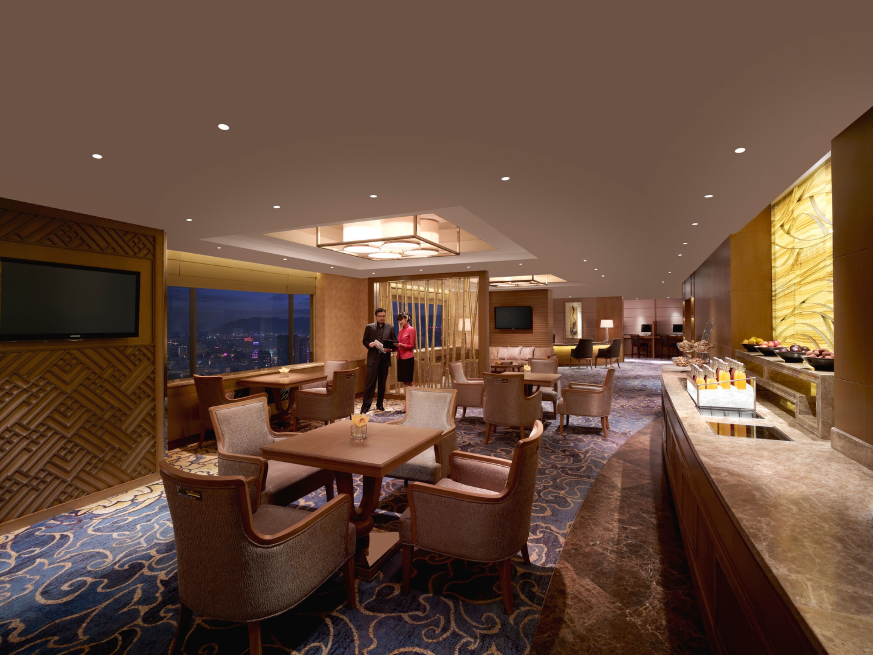 A hotel lobby with a dining area, a reception desk, and a buffet with fruit and beverages.