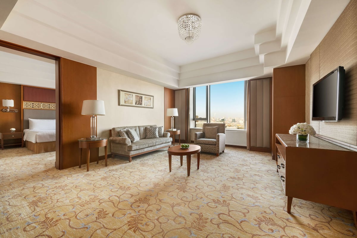 A spacious hotel room with a large bed, a sofa, a coffee table, and a TV mounted on the wall.