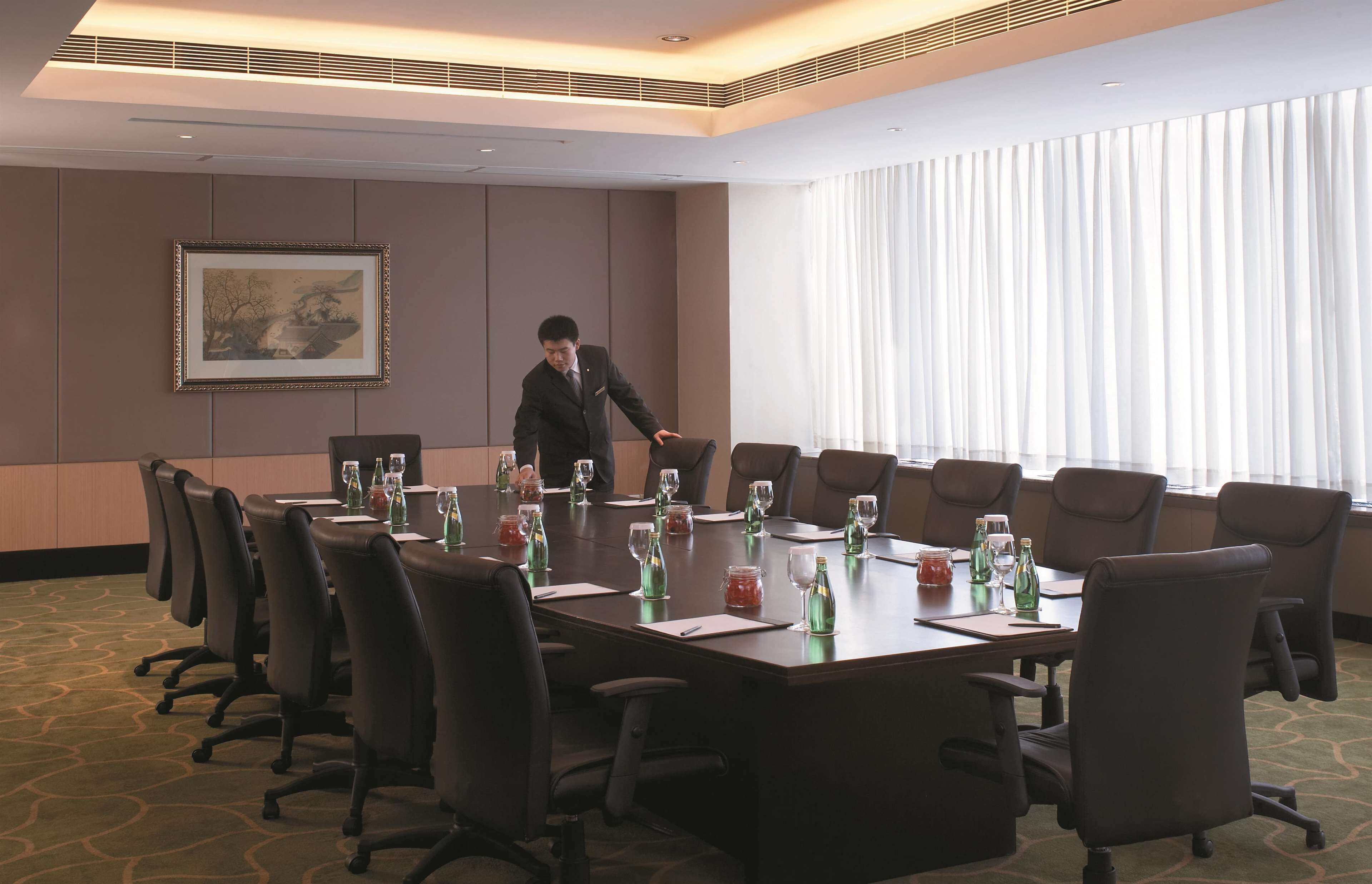 A conference room with a long table, multiple chairs, and a large window with curtains.