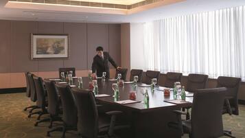 A conference room with a long table, multiple chairs, and a large window with curtains.