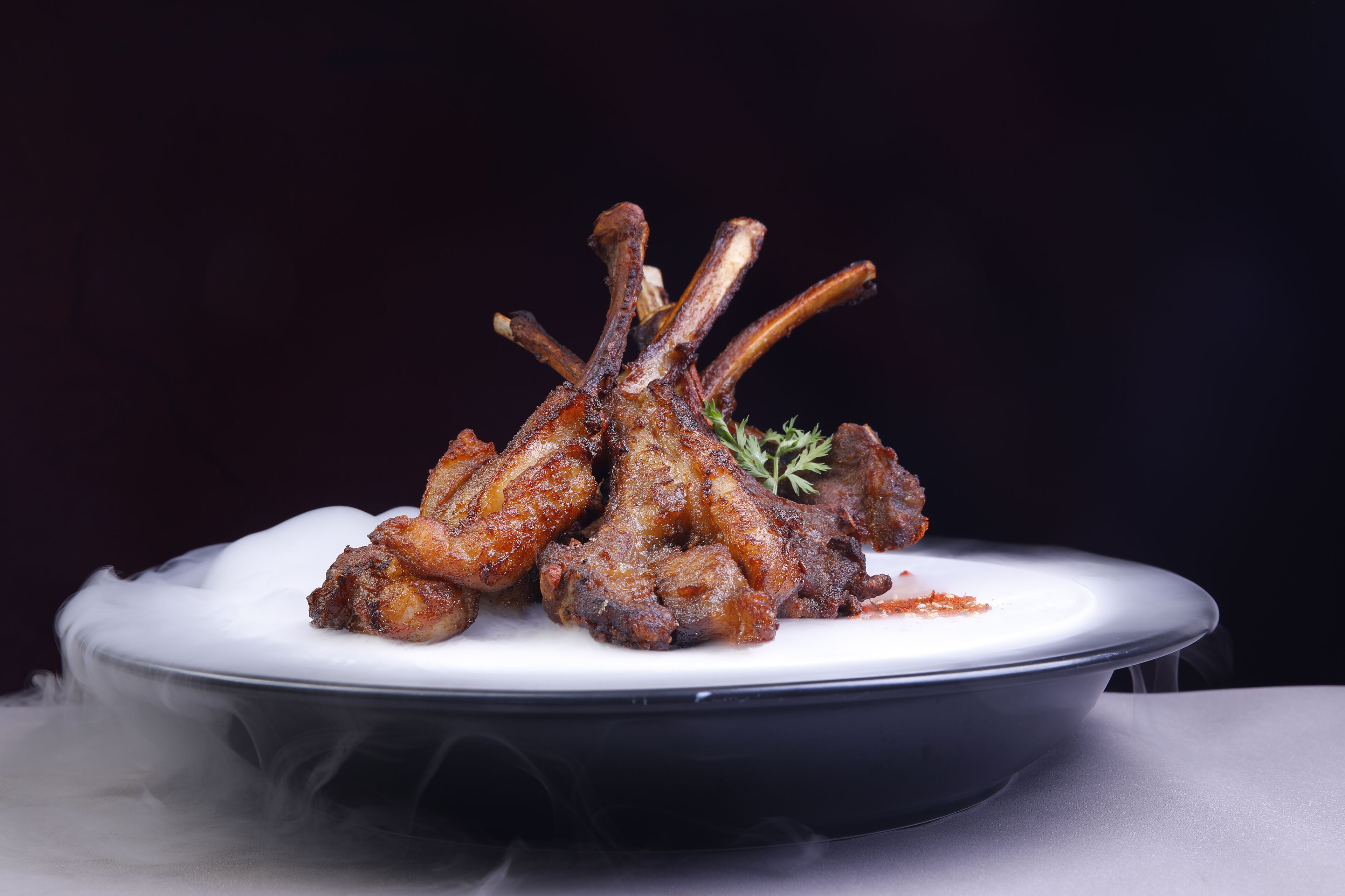 A plate of cooked lamb shanks with a garnish, served on a white plate.