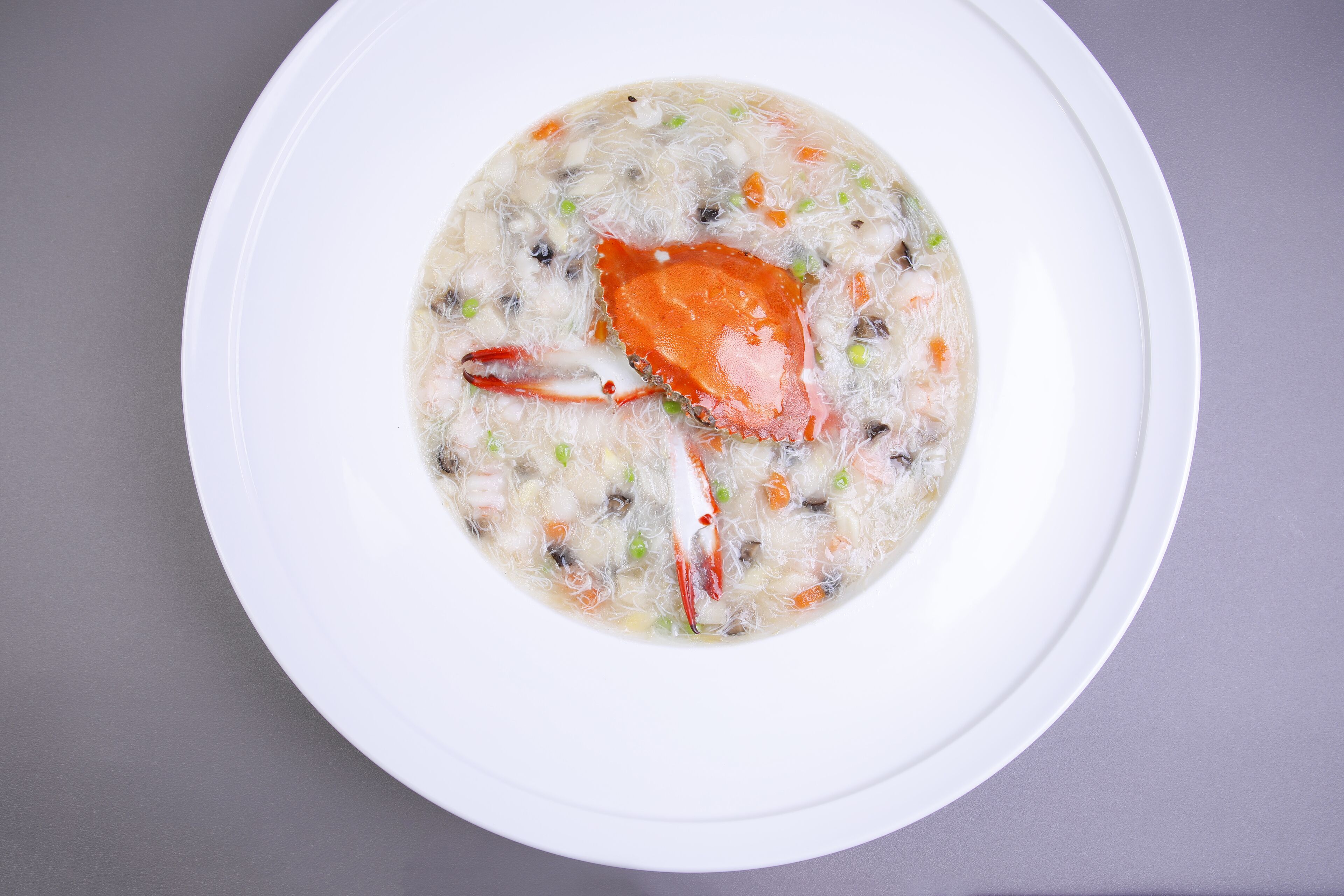Un plato blanco con una cazuela de sopa y un cangrejo.