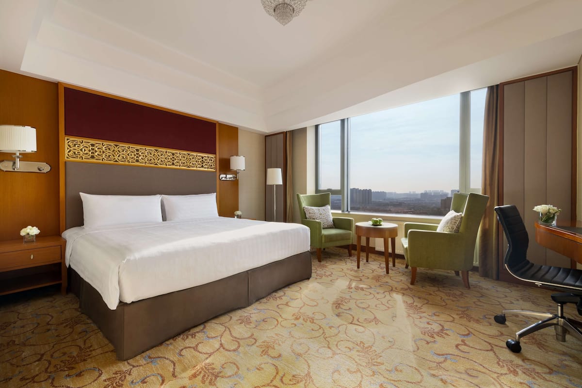 A hotel room with a large bed, a desk, two chairs, a small table, and a view of the city.