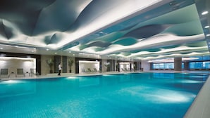 A spacious indoor swimming pool with a modern ceiling design and lounge chairs along the sides. - Shangri-La Huhhot (Hohhot)