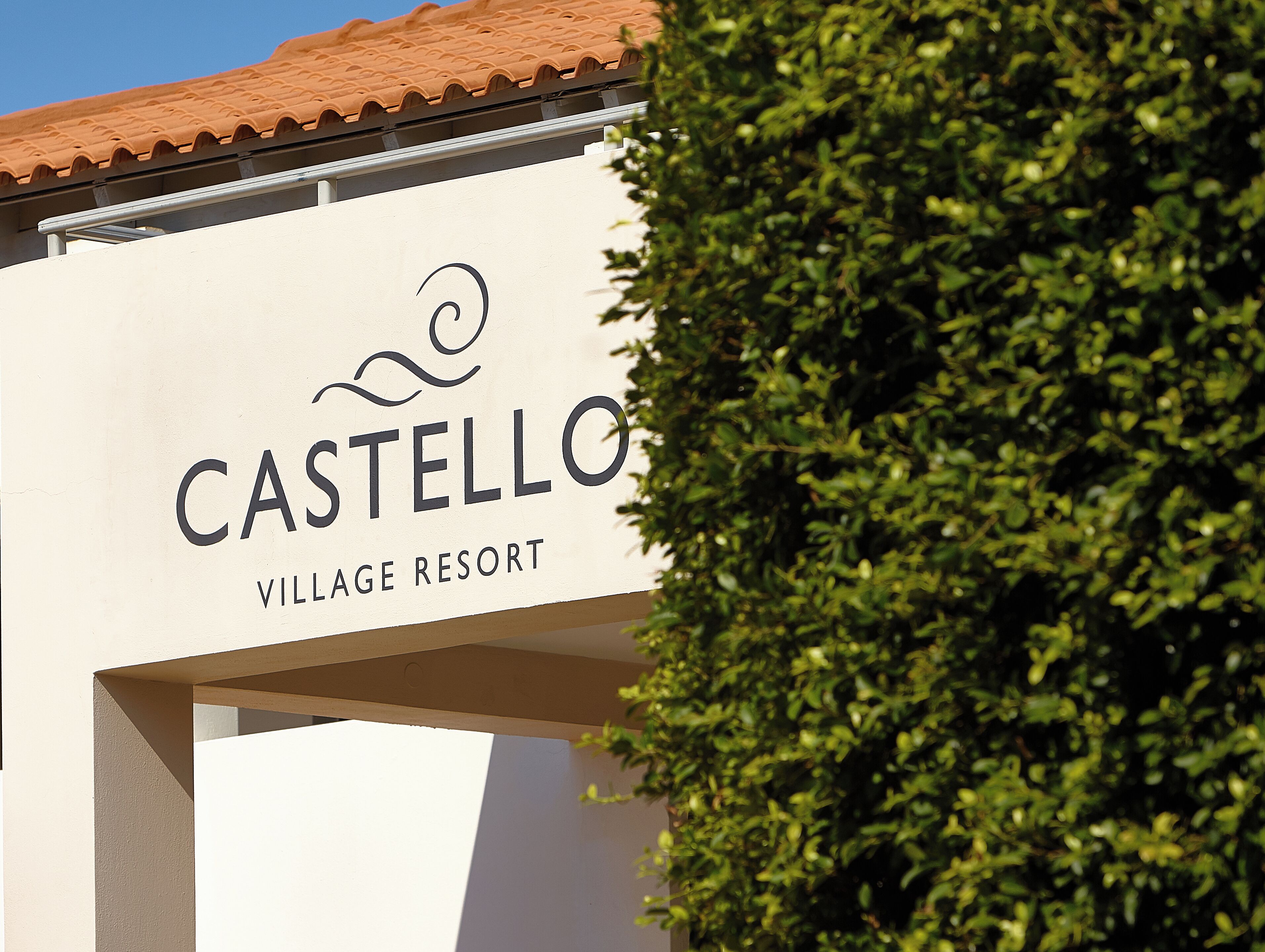 A sign for Castellò Village Resort with a clear view of the resort's name and a portion of the building's architecture.