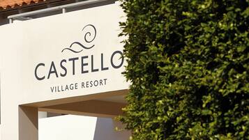 A sign for Castellò Village Resort with a clear view of the resort's name and a portion of the building's architecture.