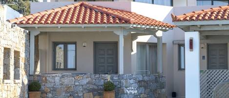 A poolside area with a stone wall, a covered patio, and a building with a tiled roof.