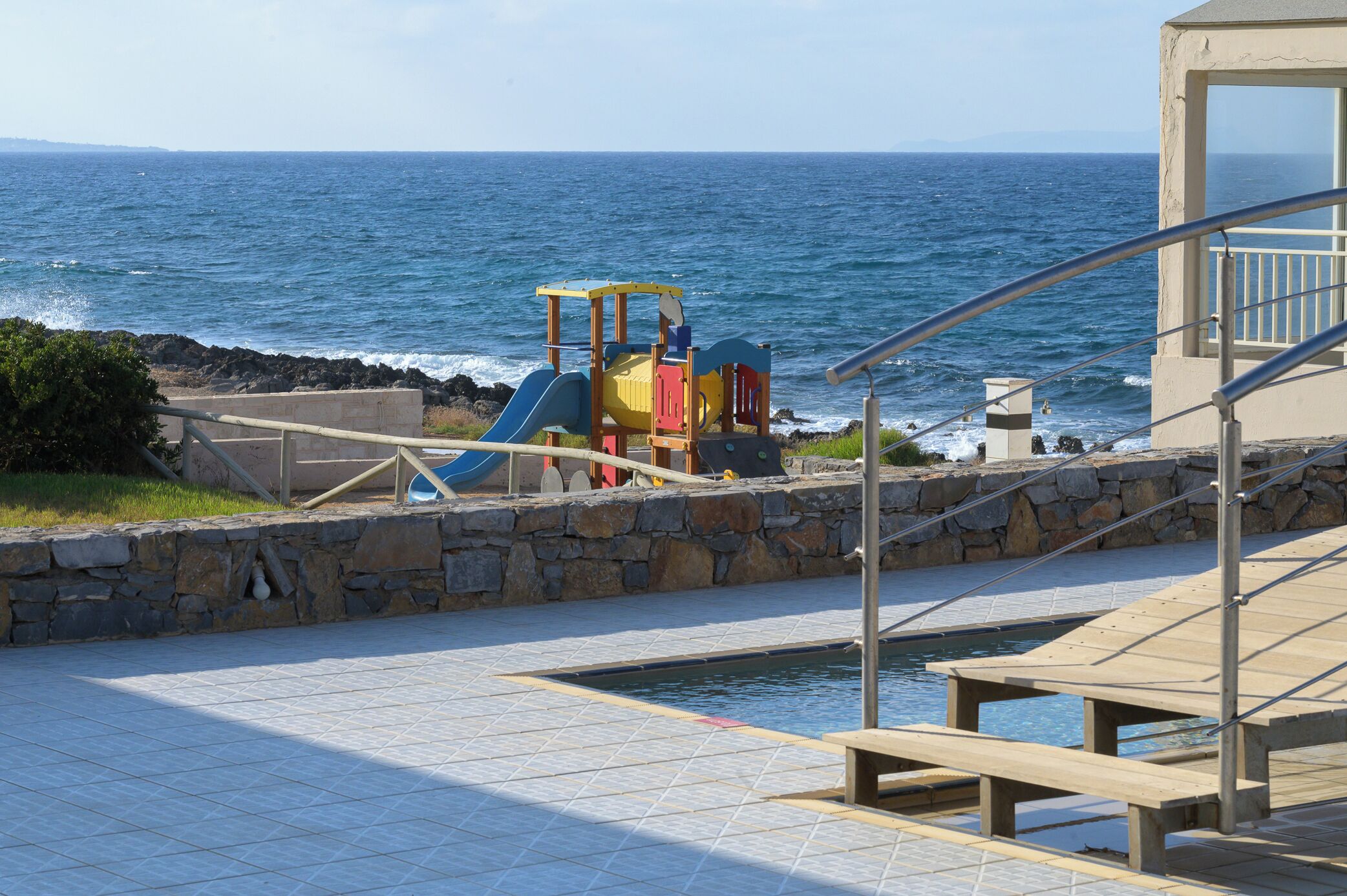 Un espace de jeux pour enfants avec un toboggan et une structure d’escalade, situé près d’une piscine et offrant une vue sur l’océan.