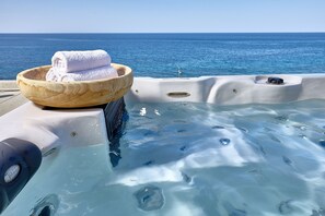 A hot tub with a wooden bowl containing towels, overlooking a body of water. - Castello Village Resort (Agios Nikolaos)