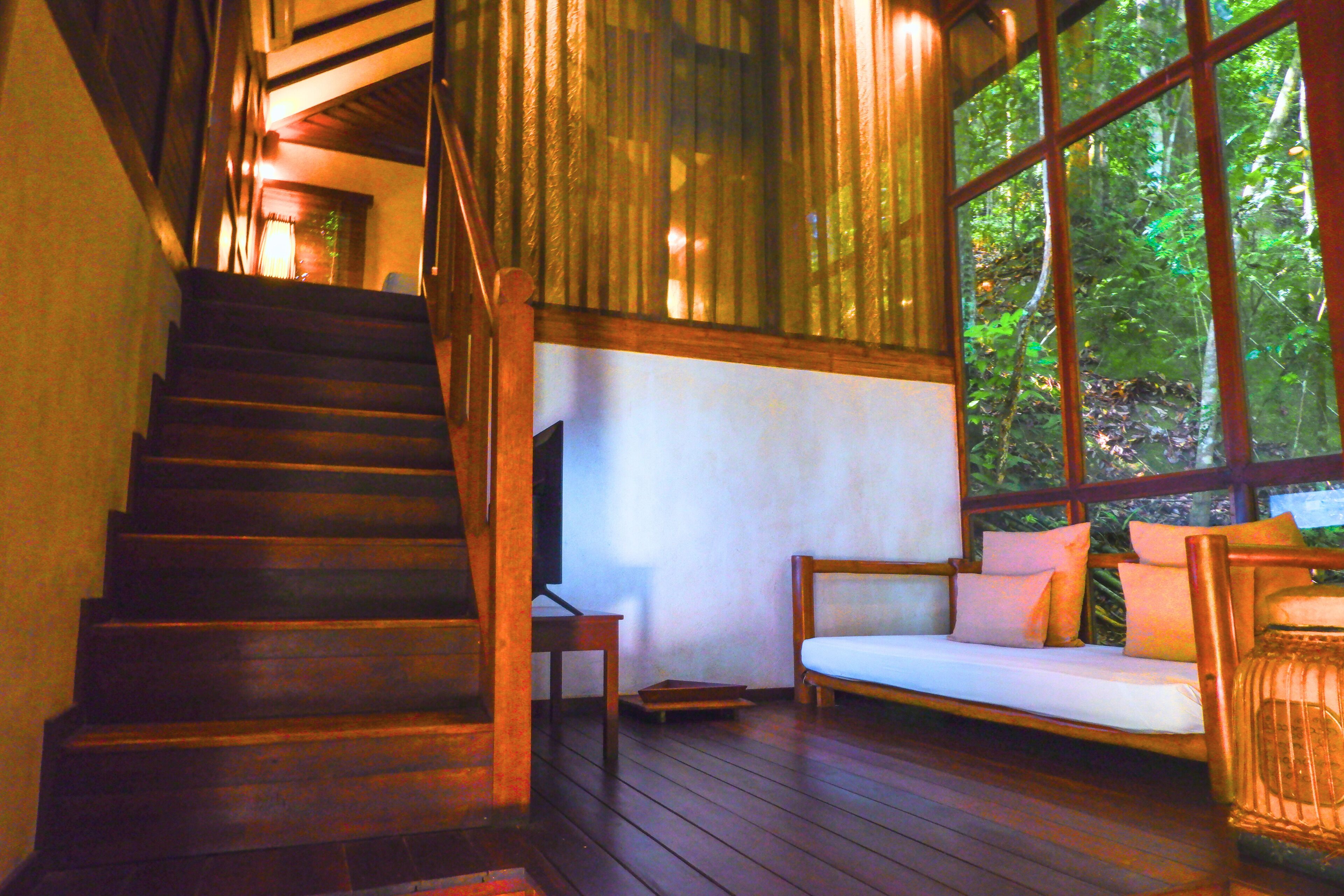 A wooden staircase leading to a room with a large window, a wooden bench, and a small table.