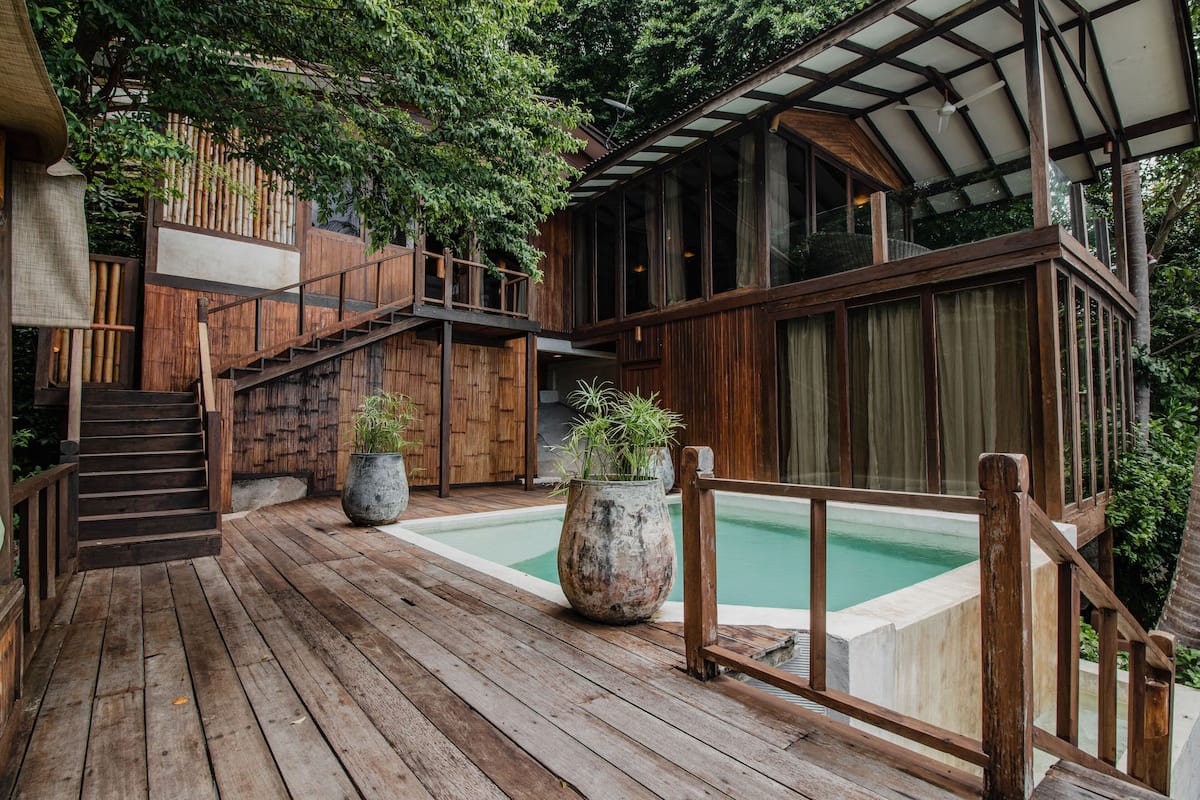 A wooden deck with a pool, wooden stairs, and a glass-enclosed area.