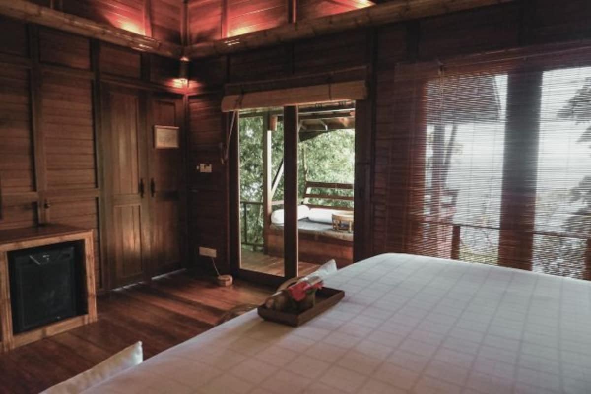 A wooden room with a bed, a small table, and a view of the outdoors.