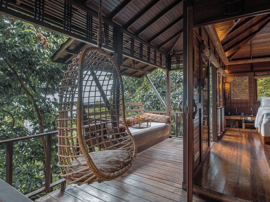 A wooden deck with a hanging chair, a sofa, and a dining table with a fruit bowl.