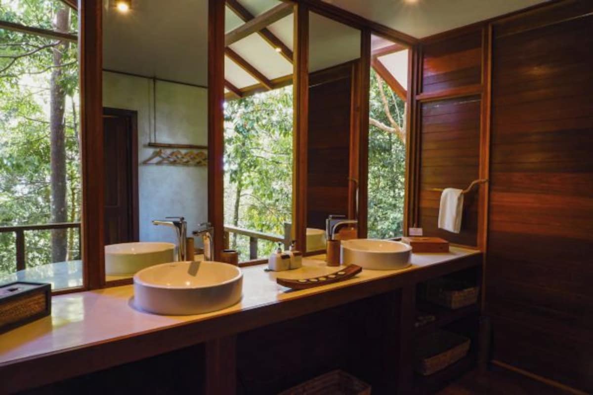 A bathroom with two sinks, wooden cabinets, and a view of greenery outside.