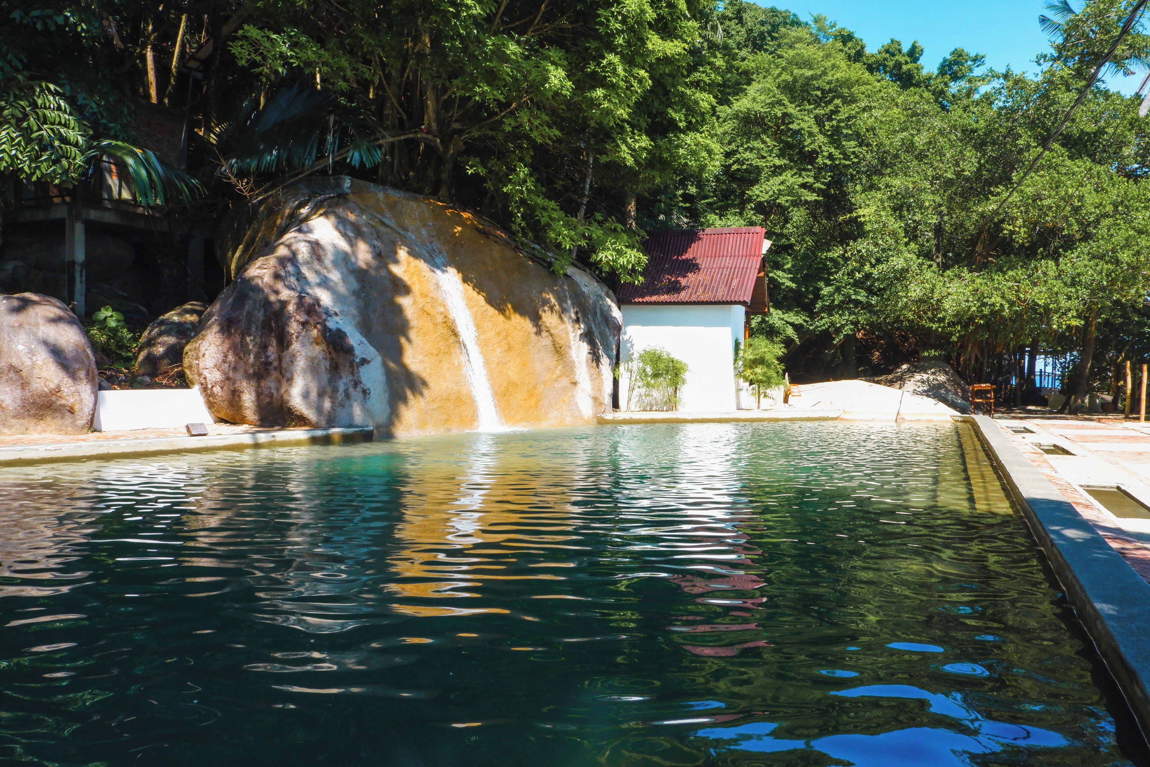 Una piscina cristalina con una cascada, rodeada de rocas grandes y vegetación exuberante.