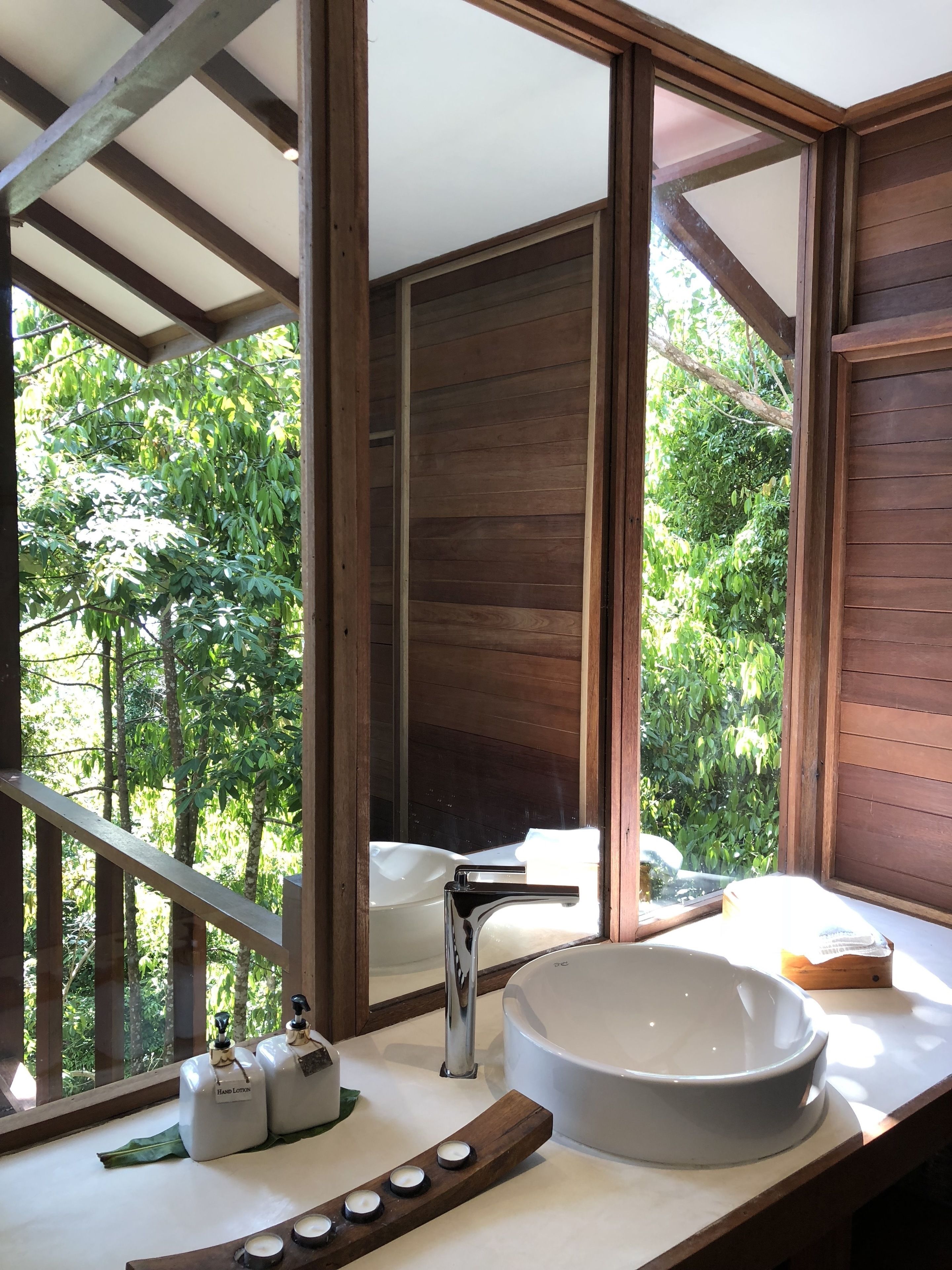 A bathroom with a large window, wooden beams, a white sink, and two hand lotion bottles.