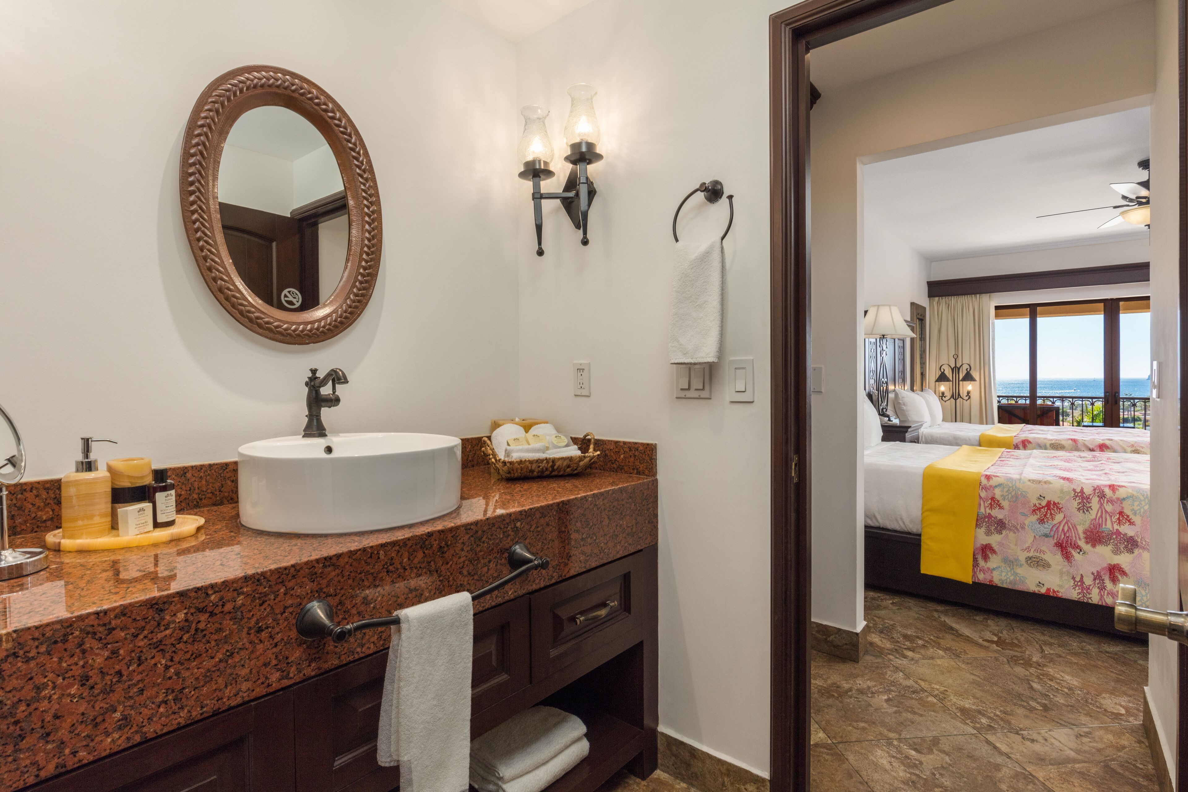 A hotel bathroom with a granite countertop, a round mirror, a sink, and a towel rack.