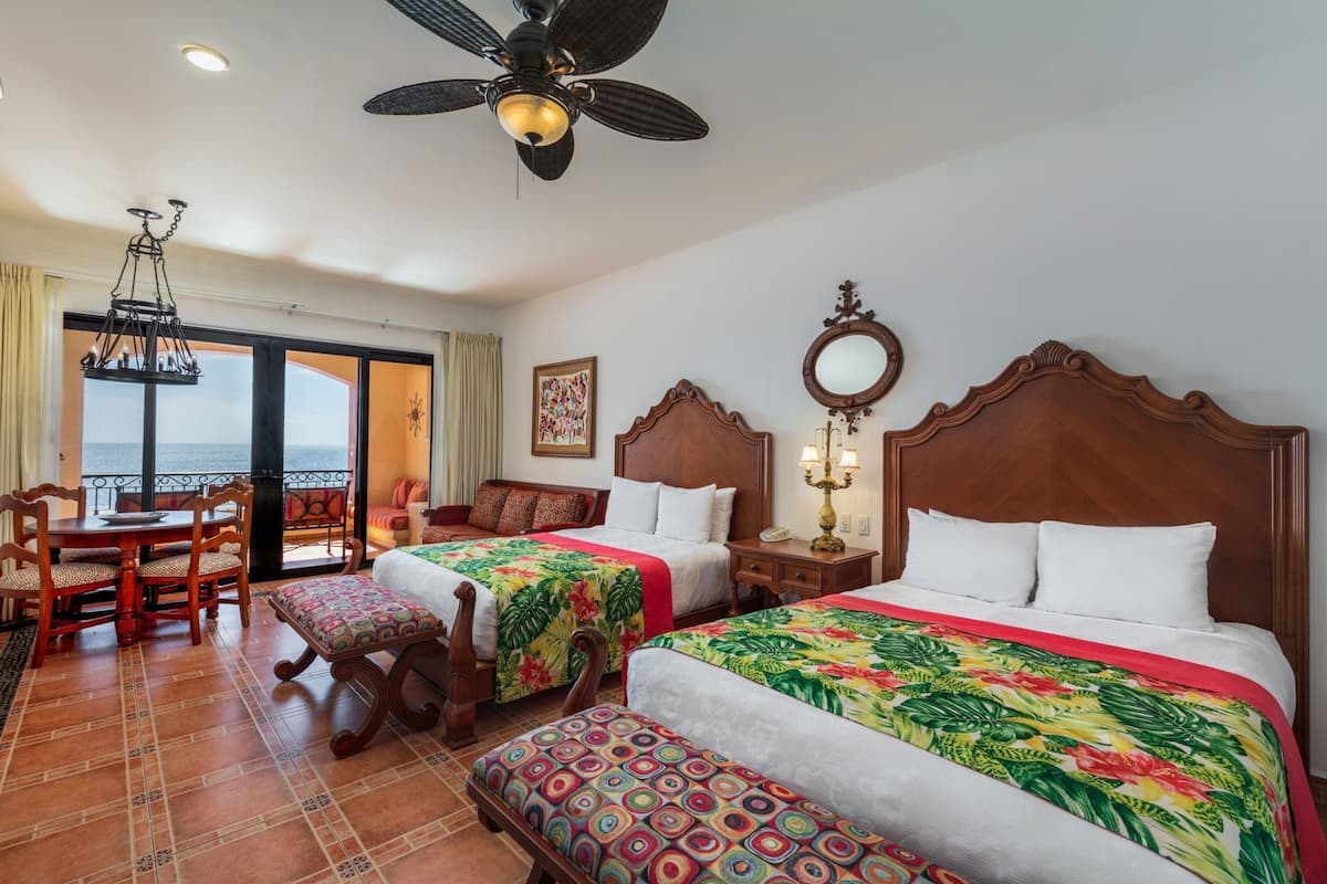 Quarto de hotel com duas camas, área de refeições, candelabro e vista para o mar.