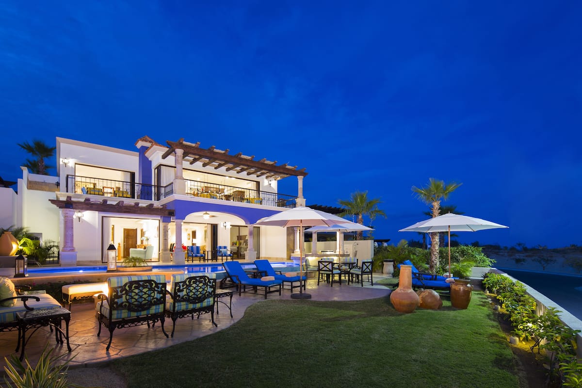 Uma casa de vários andares com área de estar externa, piscina e vista para o oceano ao entardecer.