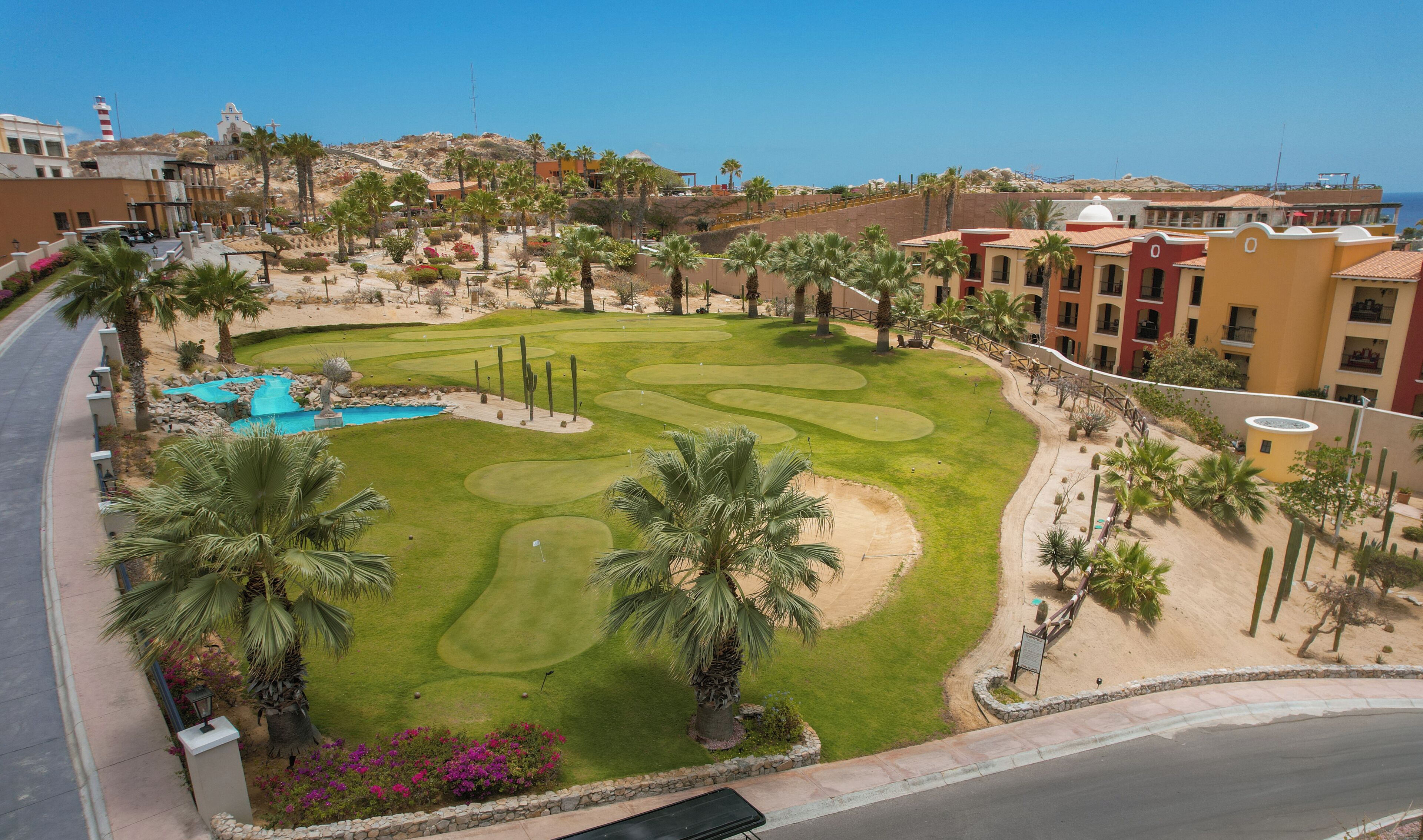 Un campo de golf con piscina, palmeras y un hotel al fondo.