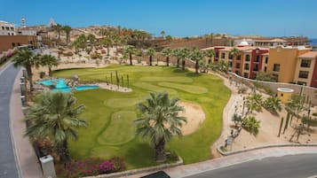Een golfbaan met een zwembad, palmbomen en een hotel op de achtergrond.