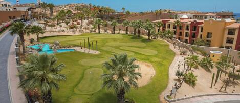 Un campo de golf con piscina, palmeras y un hotel al fondo.