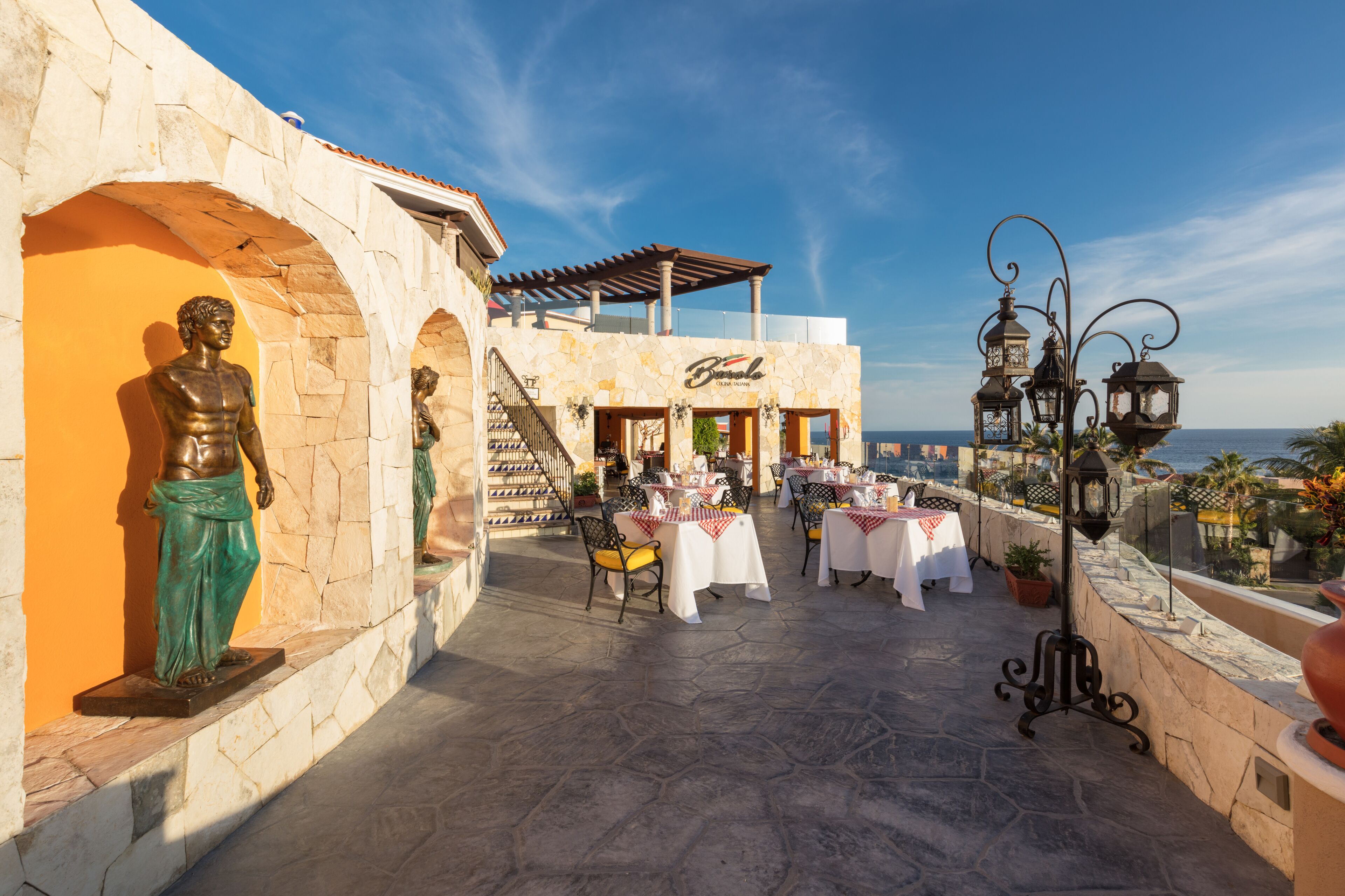 An outdoor terrace with tables and chairs, a statue, and a building with a sign.
