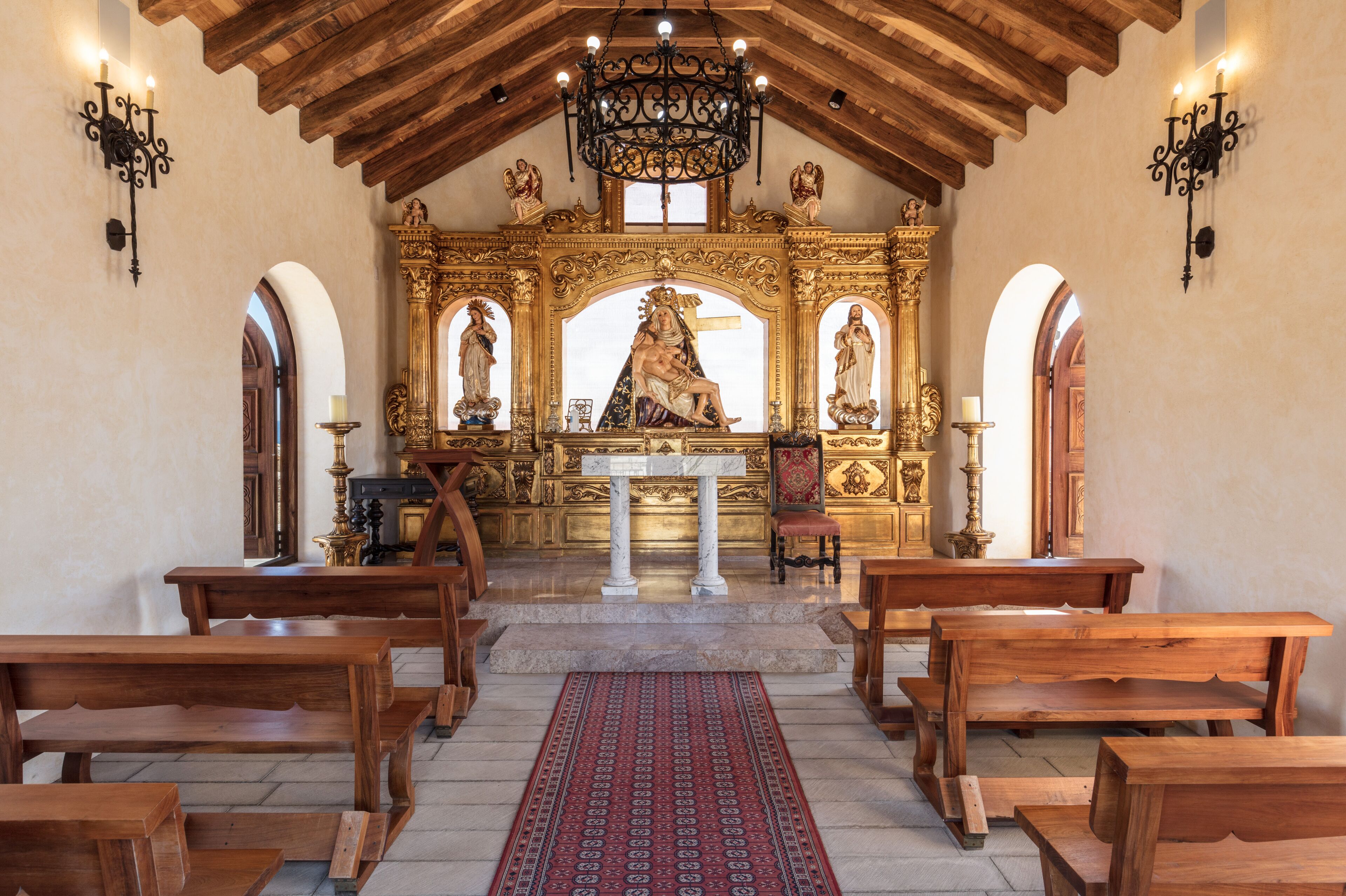 Interior com bancos de madeira, altar central e estátuas religiosas ornamentadas.