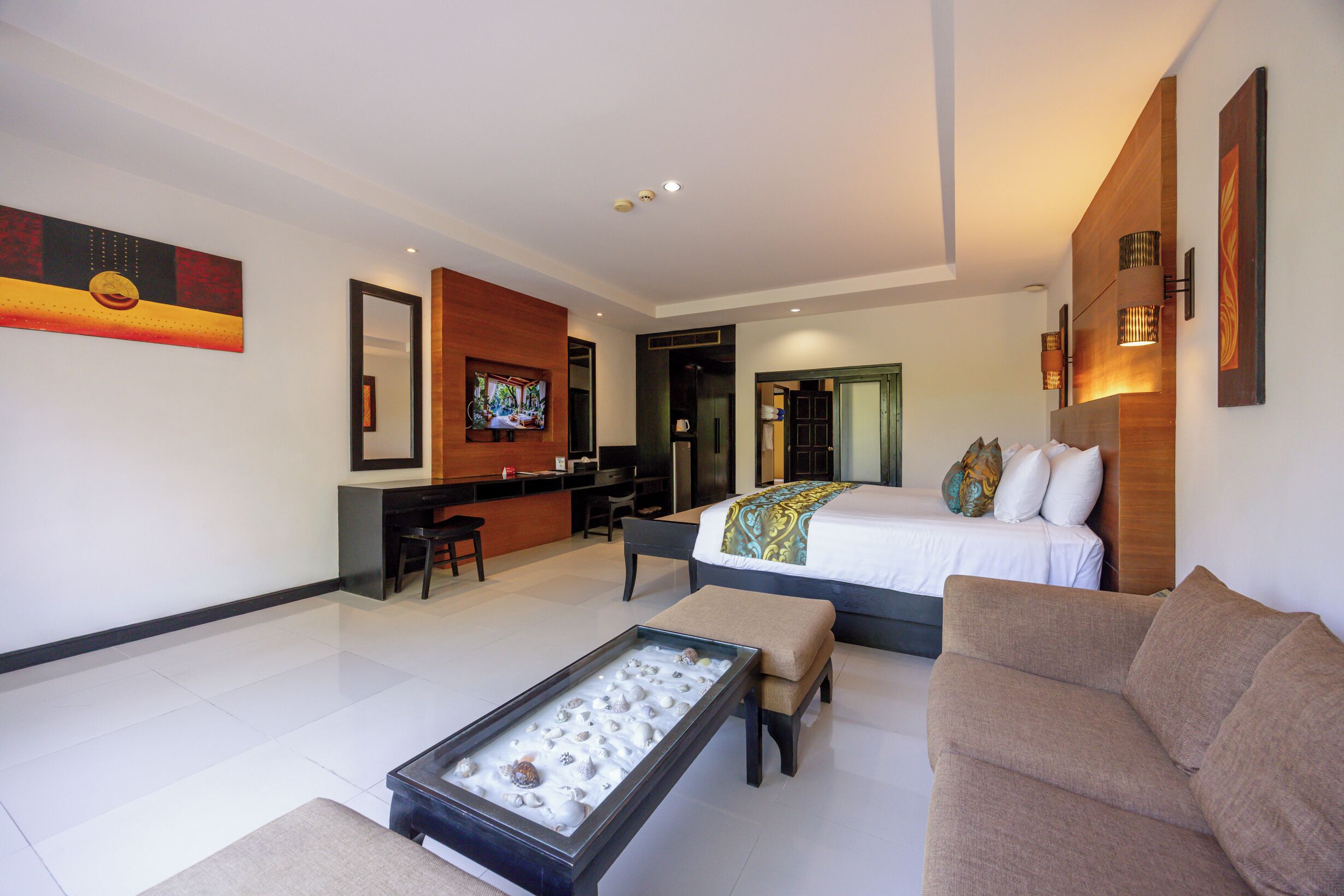 A modern hotel room with a bed, a sofa, a coffee table, a desk, and a TV.