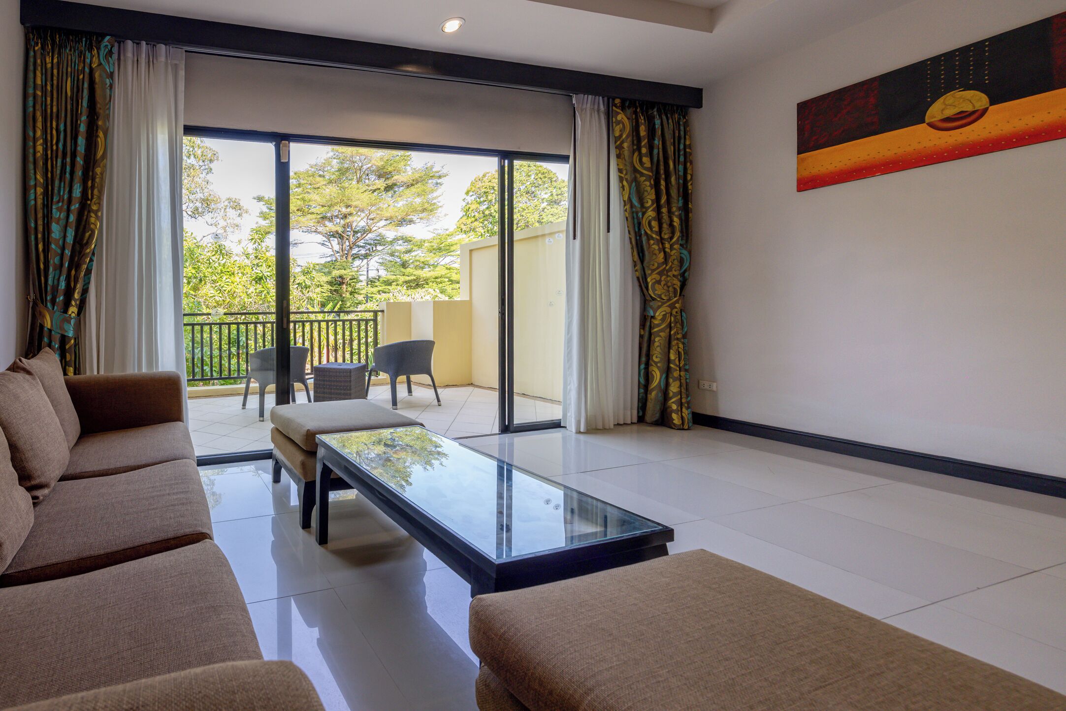 Un salon moderne avec un canapé, une table basse en verre et une vue sur un balcon aménagé avec du mobilier d’extérieur.