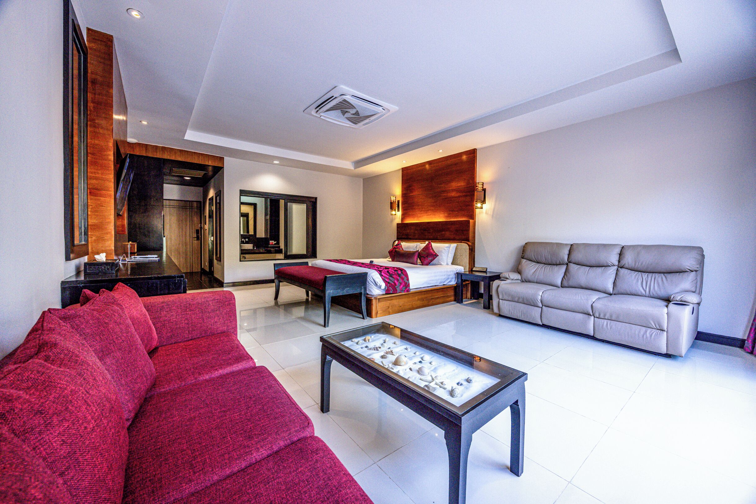 A modern hotel room with a bed, a red sofa, a grey sofa, and a coffee table.