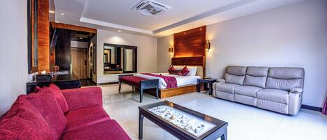 A modern hotel room with a bed, a red sofa, a grey sofa, and a coffee table.