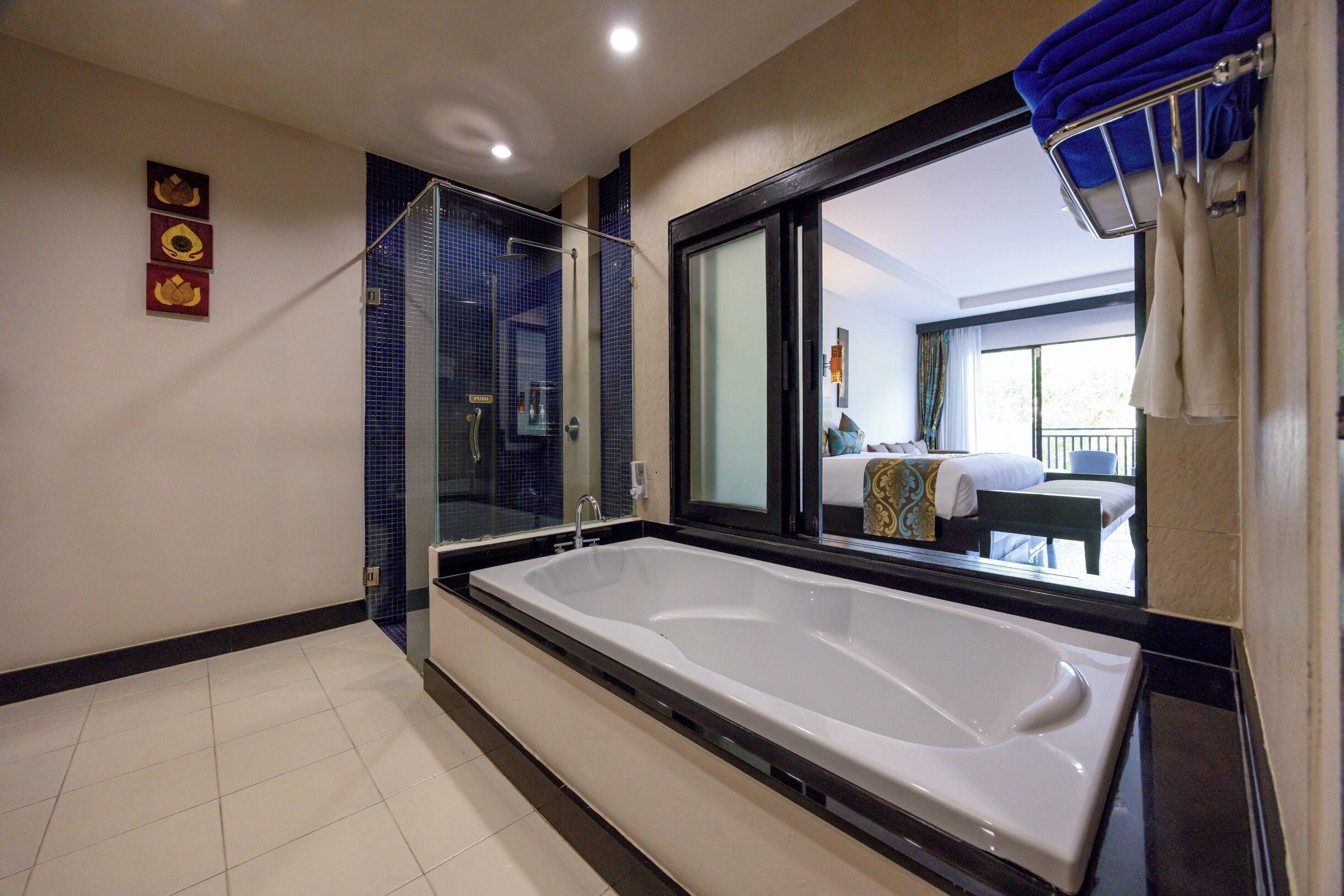 A modern bathroom with a large bathtub, a glass shower enclosure, and a view of a balcony with outdoor furniture.