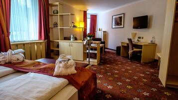 A hotel room with a bed, a desk, a chair, a television, and a carpeted floor.