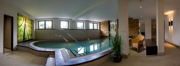 Ein moderner, überdachter Swimmingpool mit Glasabdeckung, einer Steinwand und einem Korbstuhl in der Nähe.