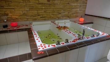 Un'area benessere con una vasca da bagno ampia, petali di rosa sul pavimento e una parete in pietra sullo sfondo.