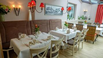 A dining area with tables set for two, a brown upholstered bench, and red wall sconces.