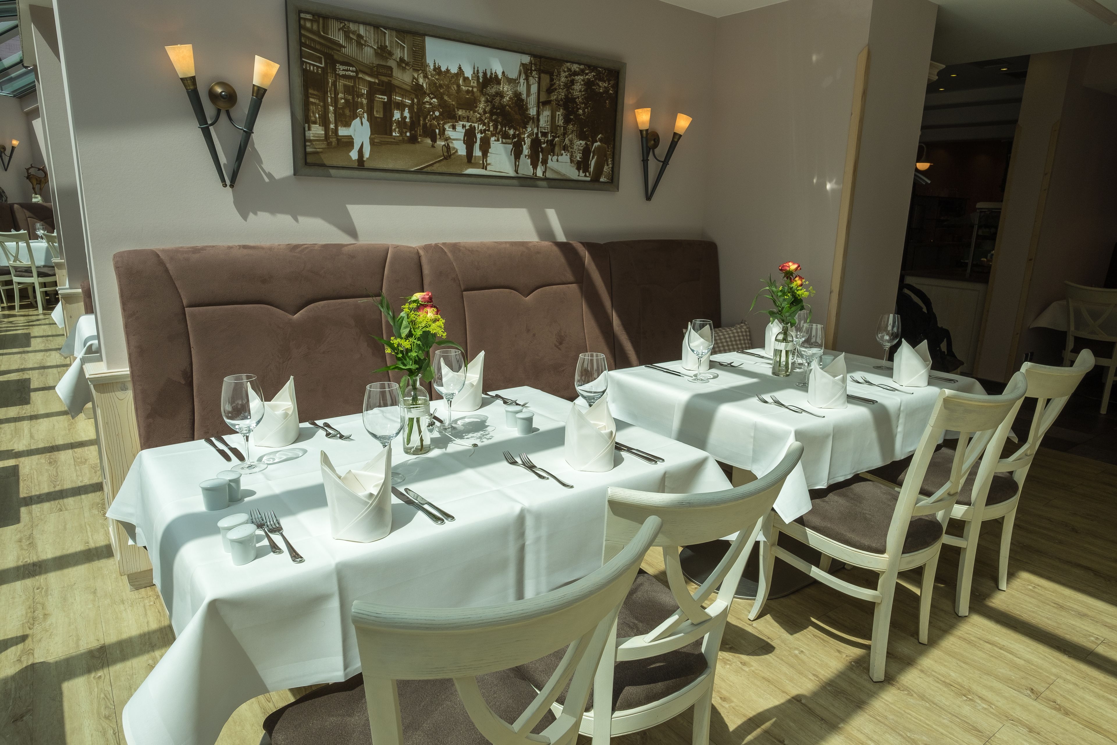 Un restaurant avec des tables recouvertes de nappes blanches, des sièges rembourrés de couleur marron et des luminaires fixés aux murs.