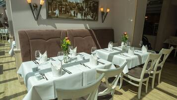 Un restaurant avec des tables recouvertes de nappes blanches, des sièges rembourrés de couleur marron et des luminaires fixés aux murs.