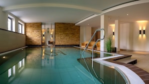 Ein moderner, überdachter Schwimmbereich mit klarem Wasser, Steinwänden und einer Glasbrüstung.