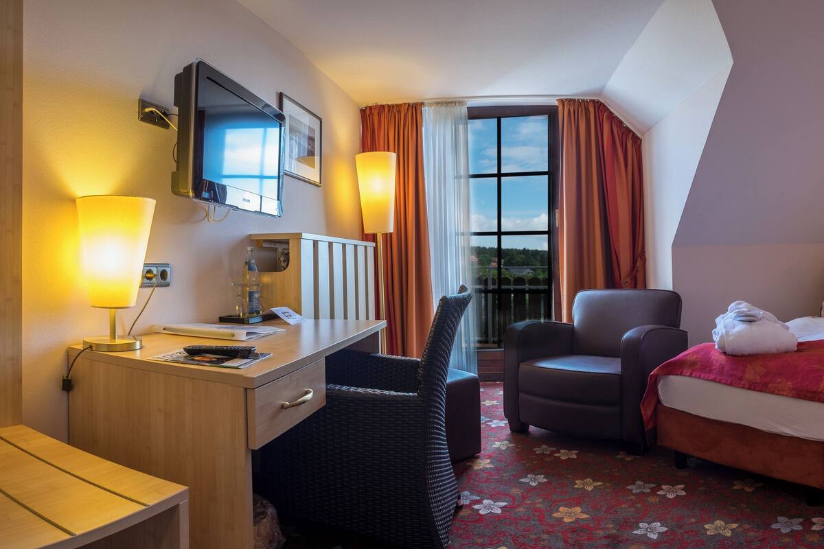 Een hotelkamer met een bed, een bureau, een stoel, een televisie en een raam met gordijnen.