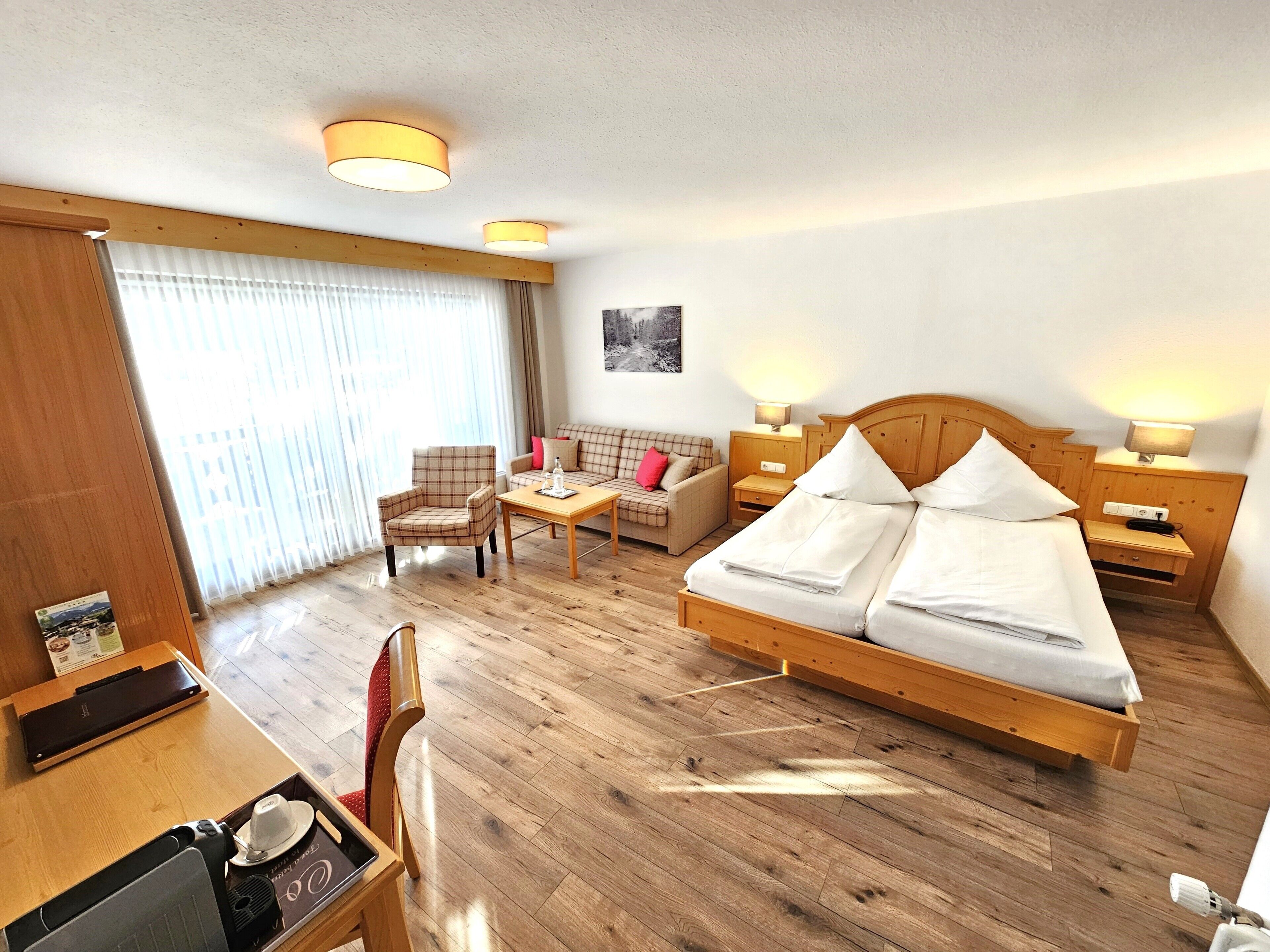 A hotel room with a wooden bed, a wooden desk, a chair, a sofa, and a table.