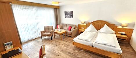 A hotel room with a wooden bed, a wooden desk, a chair, a sofa, and a table.
