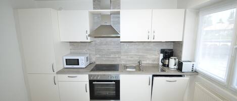 A compact kitchen with white cabinets, a built-in oven, a microwave, a coffee maker, and a sink.