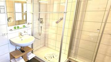 Ett modernt badrum med en dusch som är avskärmad med glasväggar, ett handfat med spegel och en hylla med toalettartiklar.
